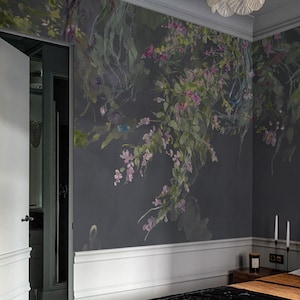 Puede incluir: Una pared de dormitorio con un mural floral gris oscuro con acentos rosas y verdes. Se ven molduras blancas y una cama marrón con una manta negra. Una lámpara de araña cuelga del techo y una puerta está entreabierta.