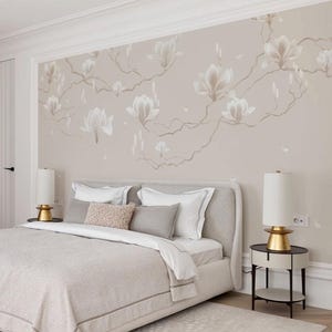 Puede incluir: Un dormitorio con una cama con cabecero y ropa de cama de color gris claro. La pared está adornada con un mural floral en tonos neutros. Dos mesitas de noche con lámparas doradas flanquean la cama y una alfombra estampada está en el suelo.