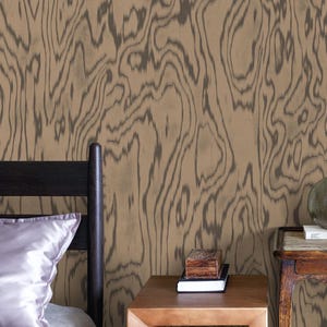 Puede incluir: Interior de dormitorio con papel pintado de vetas de madera en tonos marrón y gris. Se ve una cama con una almohada de satén, junto a una mesita de noche de madera con libros y una pequeña caja de madera. Ambiente rústico.