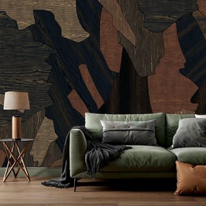 May include: A sage green sofa with a dark gray throw blanket and two pillows, one rectangular with buttons and one square. Beside it, a small table holds a lamp with a cylindrical base and a textured shade against a wood-patterned wall.
