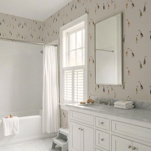 a bathroom with a white bathtub, a white sink with a mirror above it, and a white cabinet below the sink. The walls are covered in a patterned wallpaper with ducks and other birds.