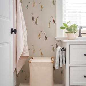 a bathroom with a white door, a white towel rack, a white trash can, and a white cabinet. The wall behind the cabinet has a pattern of ducks on it.