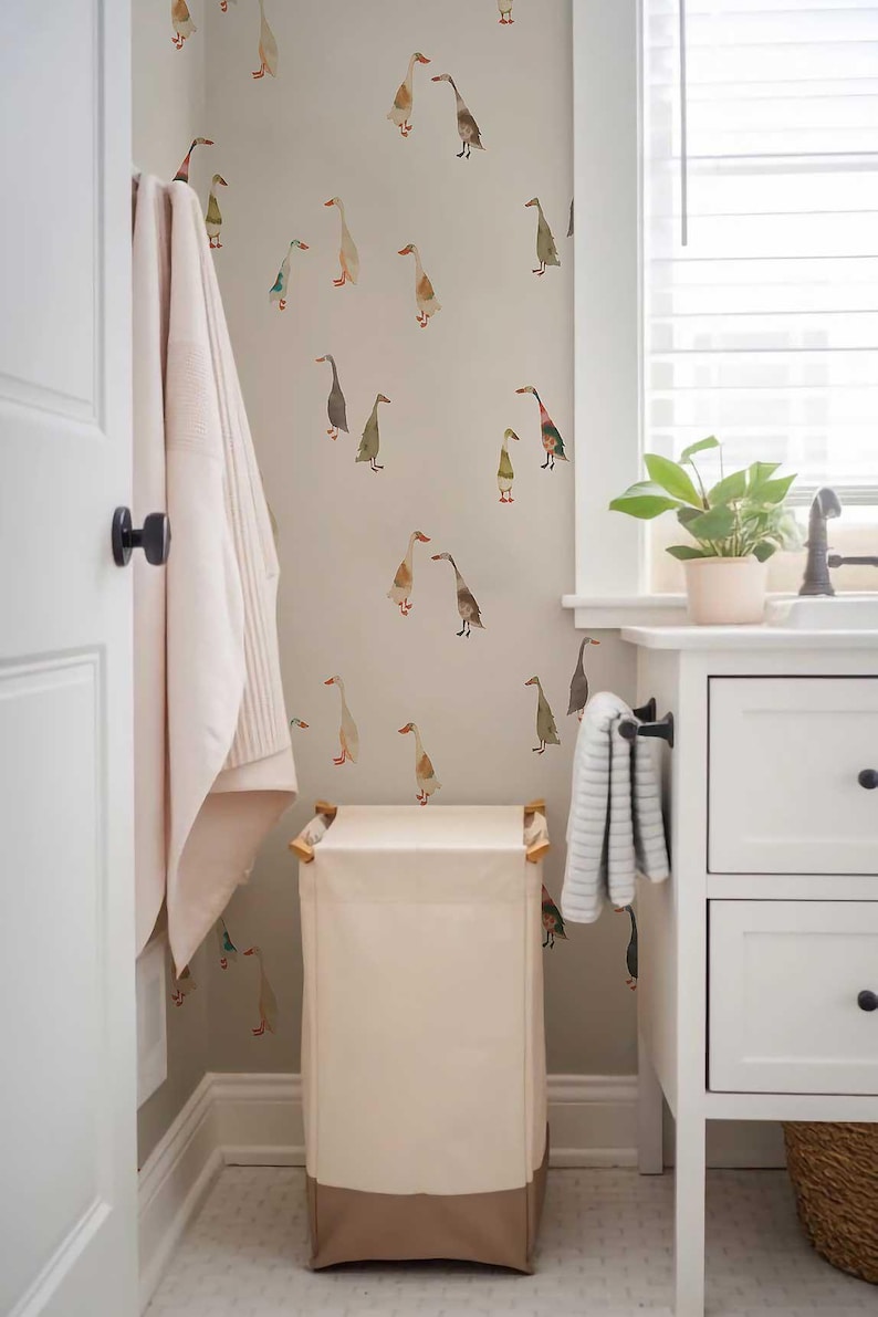 a bathroom with a white door, a white towel rack, a white trash can, and a white cabinet. The wall behind the cabinet has a pattern of ducks on it.