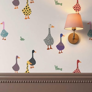 May include: Wall decals featuring a pattern of stylized geese in various colors and patterns, including polka dots, floral prints, and solid shades. The geese are arranged on a light background, interspersed with small green grass-like shapes.
