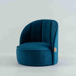 Op de afbeelding: Een lage, ronde vloerstoel bekleed met diepblauwe fluwelen stof. De rugleuning is voorzien van verticale stiksels en aan de rechterkant van de afgeronde zitting bevindt zich een klein, rechthoekig stoffen label.