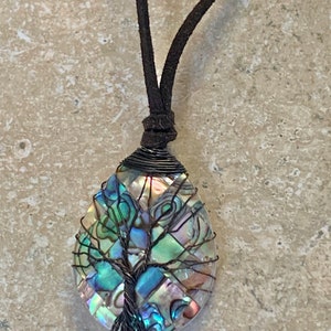 Peut inclure: Un collier avec un cordon en cuir marron et un pendentif représentant un arbre de vie en nacre d'ormeau et en fil de fer.