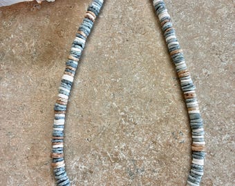 Puede incluir: Un collar compuesto por pequeñas cuentas circulares y planas en tonos azul, blanco y bronceado. Las cuentas están ensartadas en un patrón repetitivo y el collar cuenta con un cierre de langosta de metal plateado con una cadena ajustable.