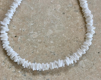 Op de afbeelding: Een witte schelpenketting gemaakt van kleine, platte, witte schelpen. De ketting is aan elkaar geregen met een simpele knoop.