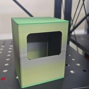 May include: A green and gray 3D printed box with a rectangular opening. The box has a gradient color effect, transitioning from green to gray.