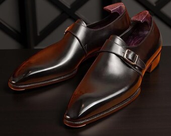 May include: Two black leather formal shoes with a single buckle strap. The shoes have a pointed toe and a polished finish.