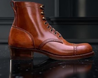 May include: A brown leather boot with a cap toe and lace-up closure. The boot has a stacked heel and a pull tab at the back. The leather has a polished finish, and the boot is set against a dark background.