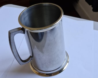 Caneca de estanho com detalhes em latão, base de latão e fundo de vidro.