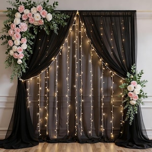 Peut inclure: Rideaux noirs transparents drapés avec des guirlandes lumineuses et des compositions florales. Les fleurs sont des roses roses et blanches avec un feuillage vert, créant un cadre romantique pour les événements.