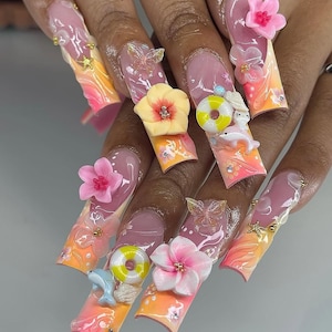 May include: Long, sculpted acrylic nails with a gradient design in shades of pink, orange, and yellow. Each nail features 3D embellishments including flowers, butterflies, dolphins, and miniature life preservers. Some nails have gold star and gem accents.