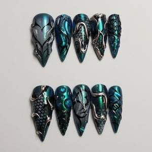 May include: A set of ten stiletto-shaped press-on nails featuring a metallic teal and dark blue color palette. The designs include raised silver liquid-like accents, black honeycomb patterns, and translucent blue spheres on a glossy finish.