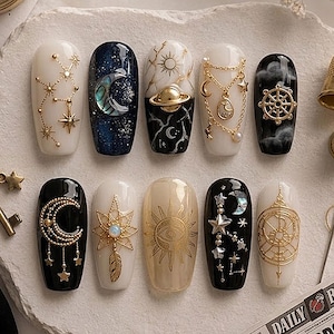May include: A set of ten press-on nails featuring celestial designs. The nails display black, white, and cream bases adorned with gold-toned metal charms, including moons, stars, planets, suns, and chains, alongside iridescent shell accents.