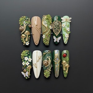 Op de afbeelding: Een verzameling van tien lange, amandelvormige kunstnagels. Elke nagel heeft een uniek ontwerp met op de natuur geïnspireerde elementen zoals slakken, paddenstoelen, vlinders, bladeren en libellen. Het kleurenpalet omvat tinten groen, beige en goud, met ingewikkelde details.