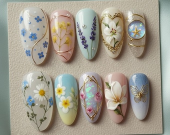 May include: A collection of ten oval-shaped, manicured fingernails with various floral and decorative designs. The nails feature a range of colors, including white, pink, blue, and gold, with detailed artwork of flowers, butterflies, and geometric patterns.