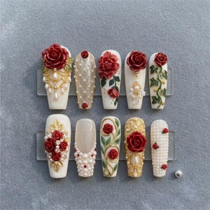 May include: A set of ten artificial nails, each with a unique design. The nails are primarily white, adorned with red roses, gold accents, and pearl embellishments. Some nails feature intricate lattice and vine patterns.
