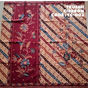 Könnte beinhalten: Ein rechteckiges Textil mit einem tiefroten Paneel auf der linken Seite mit Blumenmotiven und einem cremefarbenen Bereich auf der rechten Seite mit diagonalen Streifen und Blumenmustern. Der Text oben rechts lautet TRUSMI CIREBON CODE : TC-002.