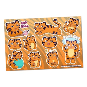 Puede incluir: Una hoja de pegatinas de tigre naranja y negro en varias poses. Algunas pegatinas tienen el texto "BAD GRRL" y "I'LL BE GOOD!". El fondo es naranja con un patrón de rayas de tigre. El sitio web www.shishidocreative.com es visible.