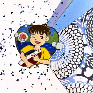 May include: A vibrant enamel pin depicting a cartoon boy with a boat. The boy is winking and smiling, with a thought bubble showing a girl and a lake scene. The pin has a yellow shirt and a blue and white background.