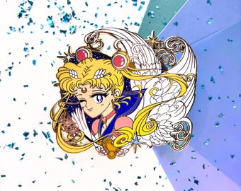 May include: A gold-colored enamel pin featuring a cartoon character with blonde hair, a pink and blue outfit, and angel wings. The pin has a winking expression and is set against a white and blue background with glitter.