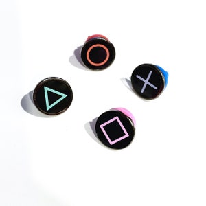May include: Four black buttons with different colored rings and symbols. The symbols are a circle, a triangle, a square, and an X.