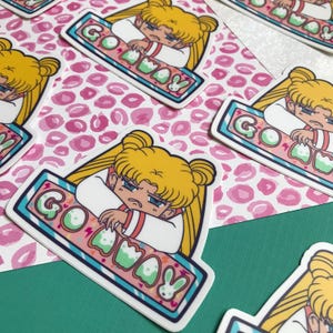 May include: A sticker featuring a cartoon character with yellow hair and a blue and white outfit. The character is sitting on a blue and white striped platform with the text "Go Away" in pink and green letters.
