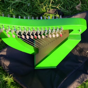 Könnte beinhalten: Eine leuchtend grüne Leier mit Saiten und Stimmwirbeln. Das Instrument steht auf einer schwarzen Oberfläche, mit grünem Gras im Hintergrund. Die Harfe hat einen dreieckigen Resonanzkörper und eine gebogene Oberseite.