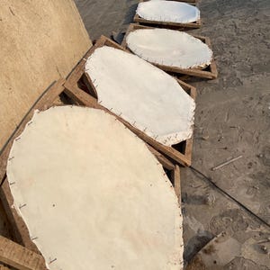 May include: Several pieces of white leather are stretched and secured with nails on wooden frames. The frames are arranged in a row on a concrete surface, likely for drying or processing. The leather has a slightly irregular shape.