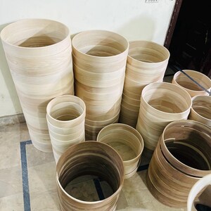 May include: A collection of unfinished wooden cylinders of varying heights and diameters. The cylinders are made of light-colored wood, with visible grain patterns. Some are stacked, while others are arranged individually. The overall aesthetic is natural and rustic.