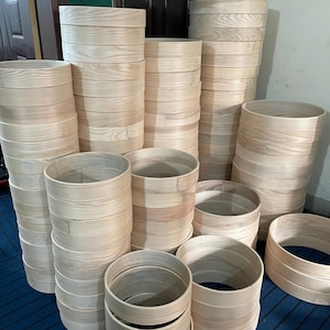 May include: A collection of unfinished wooden rings and cylinders. The natural wood grain is visible on the surfaces. The cylindrical pieces are stacked in varying heights, suggesting a craft or woodworking project. The rings are of different diameters.