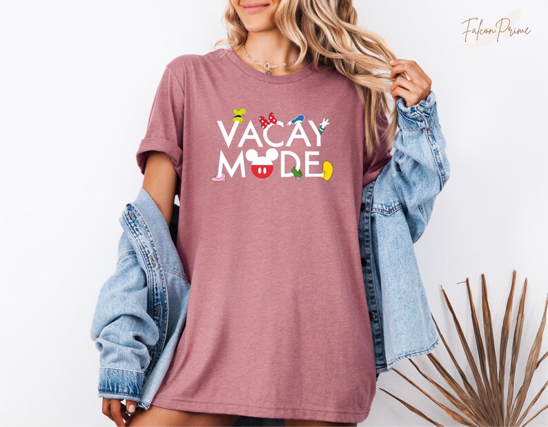 Puede incluir: Una camiseta color malva con el texto "Vacay Mode" en letras blancas. El texto est&aacute; rodeado de im&aacute;genes de dibujos animados coloridos de Mickey Mouse y otros personajes de Disney.