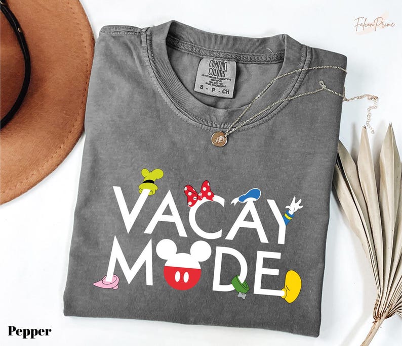 A gray t-shirt with the text "VACAY MODE" printed on it, along with various Disney character icons, is displayed on a white surface.