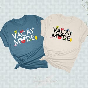Puede incluir: Dos camisetas con el texto "Vacay Mode" en letras negras con una cabeza de Mickey Mouse y otros personajes de Disney. La camiseta de la izquierda es de color azul oscuro jaspeado y la camiseta de la derecha es de color natural.