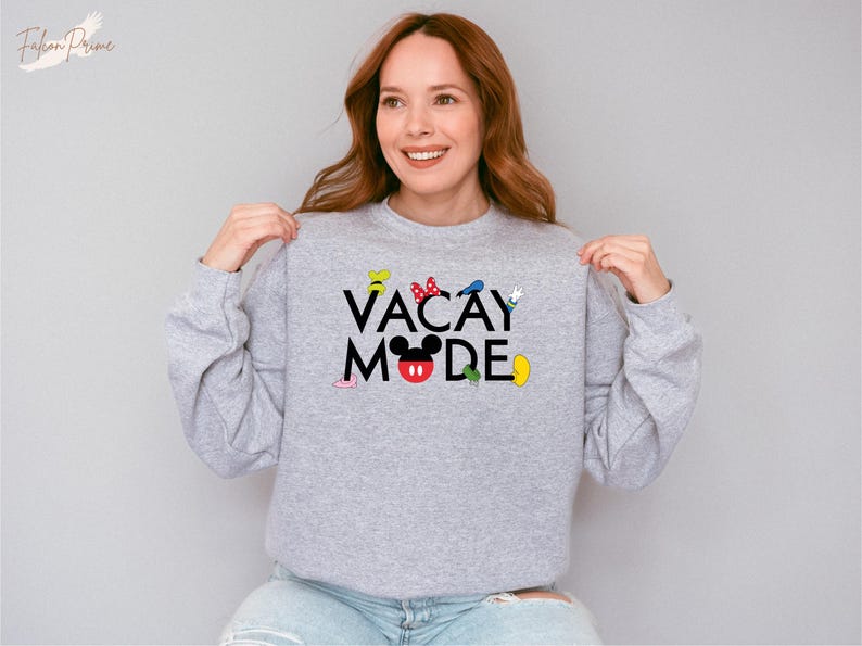 Puede incluir: Una sudadera gris con el texto "VACAY MODE" en letras negras. El texto est&aacute; rodeado de personajes de dibujos animados coloridos, incluido Mickey Mouse.