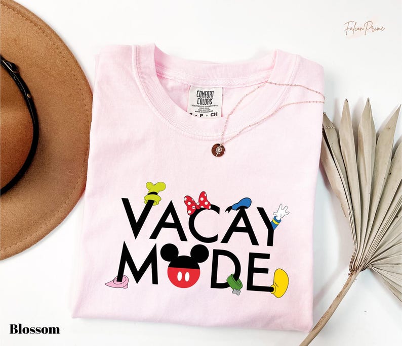 A pink t-shirt with the text "VACAY MODE" printed on it, along with various Disney character icons, is displayed on a white background.
