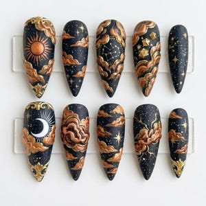May include: A set of ten almond-shaped press-on nails featuring a black base with a celestial theme. The designs include raised copper-colored clouds, a sun, a crescent moon, constellations, and gold-painted stars against a speckled night sky.