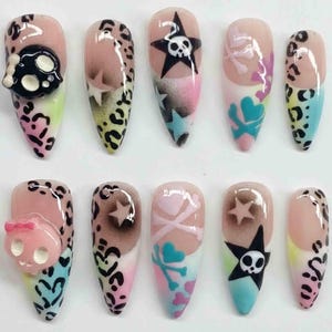 May include: A set of ten long, pointed artificial nails. Designs include leopard print, skulls, stars, hearts, and crossbones in black, pink, blue, and yellow. Some nails feature 3D skull embellishments.