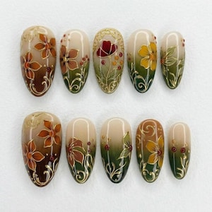 May include: A set of ten almond-shaped press-on nails featuring a gradient transition from cream to olive green. Each nail is decorated with hand-painted floral motifs in shades of orange, yellow, and red, accented with intricate gold filigree lines.