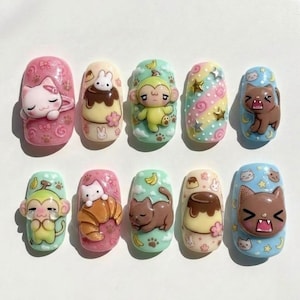 May include: A set of ten press-on nails featuring 3D resin charms of cartoon monkeys, cats, and puddings. The designs include pastel backgrounds with patterns of swirls, stars, bananas, and paw prints, showcasing various expressive character faces.