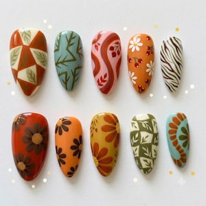 May include: A set of ten almond-shaped press-on nails featuring diverse designs including geometric leaf patterns, abstract swirls, floral motifs, berries, and zebra stripes in a warm colour palette of orange, brown, green, pink, and cream tones.