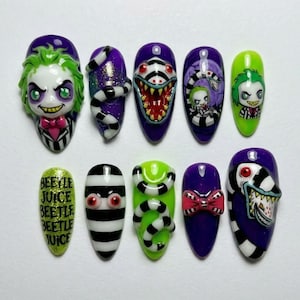 Puede incluir: Un juego de diez uñas postizas con diseños de personajes en morado, verde, negro y blanco. Las uñas muestran ilustraciones de un personaje de pelo verde, serpientes a rayas blancas y negras, una criatura de boca ancha y el texto Beetlejuice.