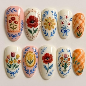 Peut inclure: Un ensemble de dix faux ongles ornés de motifs floraux peints à la main. Les ongles présentent divers dessins incluant des coquelicots rouges, des marguerites jaunes, des bouquets de tulipes multicolores et des motifs à carreaux orange.