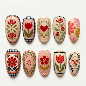 May include: A collection of ten oval-shaped nail art designs. Each nail features a different floral or heart design in red, pink, and green, with details like gingham and decorative borders. The nails are set against a white background.