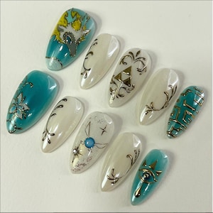 May include: A set of ten almond-shaped, professionally manicured artificial nails. The nails feature various designs, including floral patterns, geometric shapes, and stylized illustrations in teal, gold, and white. Some nails have a pearlescent finish.