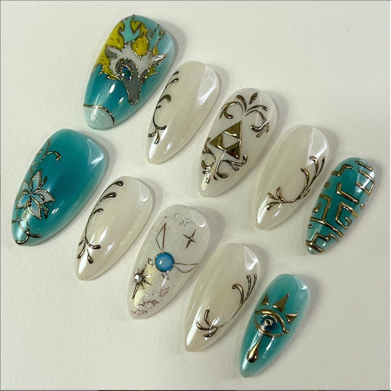 May include: A set of ten almond-shaped, professionally manicured artificial nails. The nails feature various designs, including floral patterns, geometric shapes, and stylized illustrations in teal, gold, and white. Some nails have a pearlescent finish.