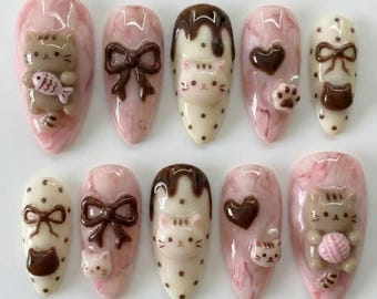 May include: A set of ten almond-shaped false nails with a pink marble effect. Each nail features 3D embellishments, including brown bows, cat faces, hearts, paw prints, and a cat holding a ball of yarn or a fish.