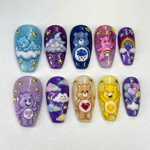 Puede incluir: Un juego de diez uñas postizas con personajes de Care Bears, nubes, arcoíris y globos. Cada uña tiene una base brillante en tonos azules, morados o amarillos, decorada con pequeñas aplicaciones doradas en forma de estrella por toda la superficie.